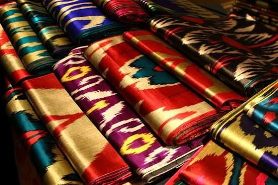 Folded lengths of Margilan ikat silk in crimson, gold and teal